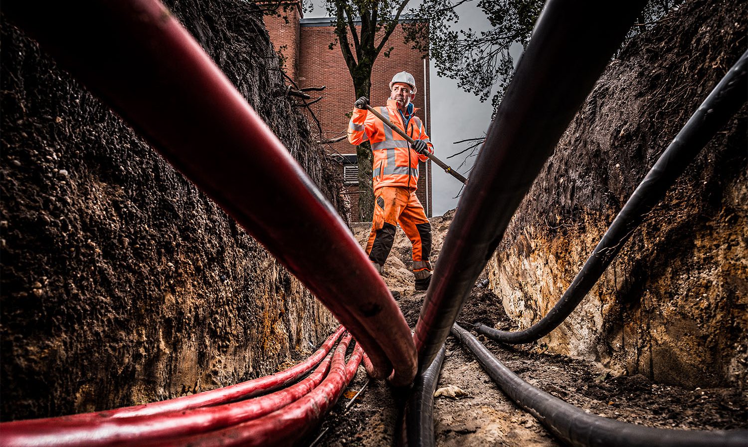 Een grondwerker aan het werk met leidingen en kabels.