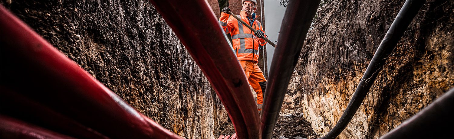 Grondwerker aan het werk tussen kabels en leidingen.