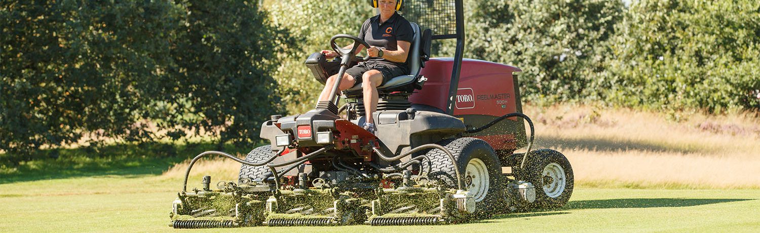 Greenkeeper op de maaimachine bezig op de golfbaan.